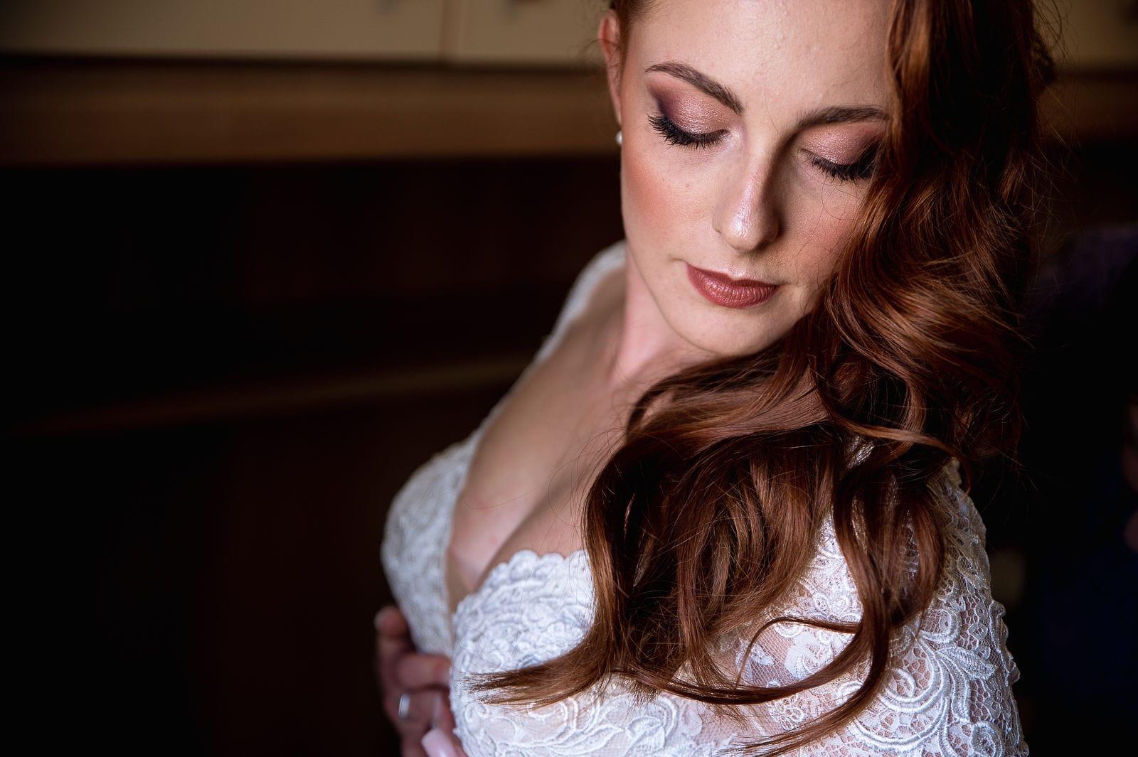 Sposa con lo sguardo abbassato, trucco morbido e capelli rossi raccolti su una spalla