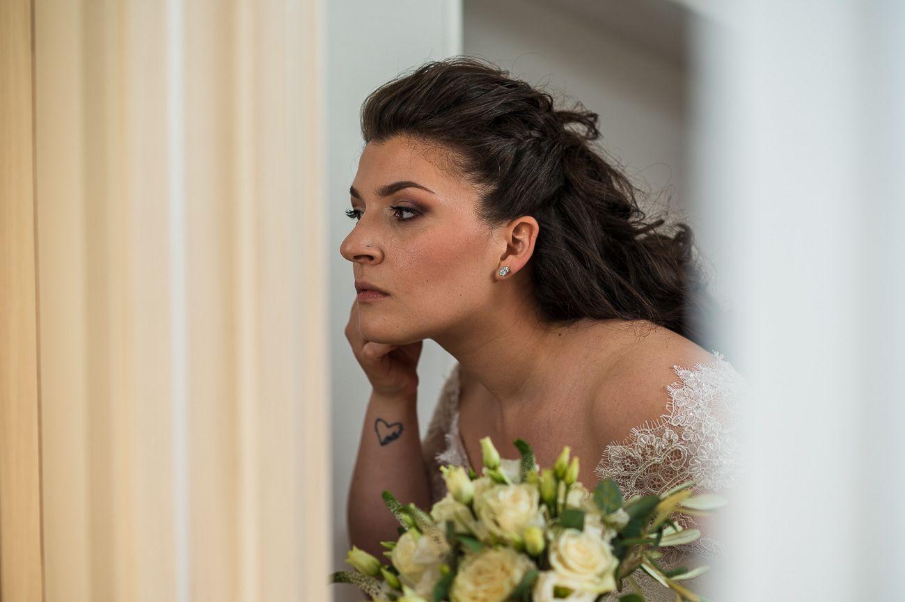 Sposa in attesa accanto a una finestra, con un bouquet di fiori bianchi