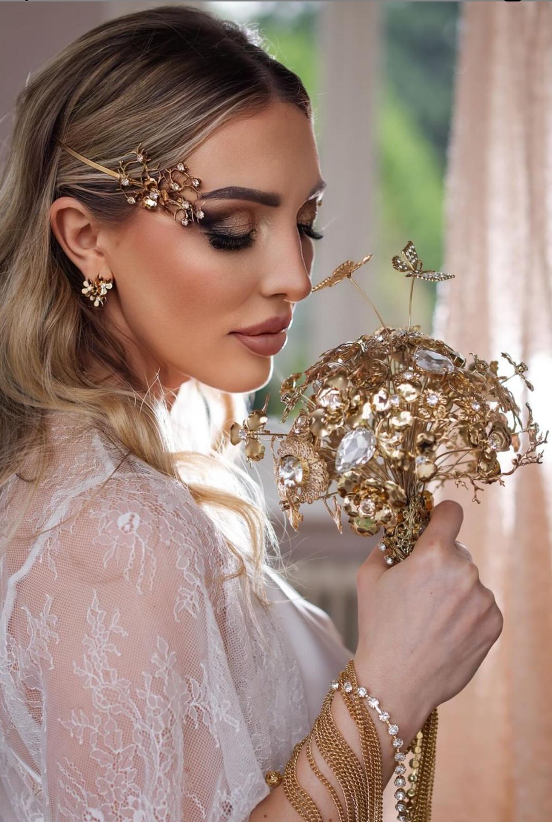 Sposa con occhi sfumati nei toni del bronzo, accessori dorati tra i capelli e bouquet gioiello